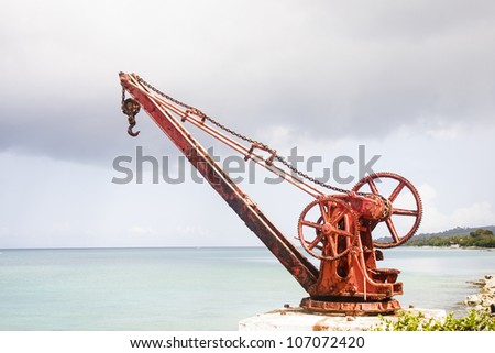 An old rusty, red crane with manual crank on the shore of a tropical island