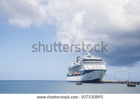 A massive luxury blue and white cruise ship at a dock in the tropics under a storm cloud
