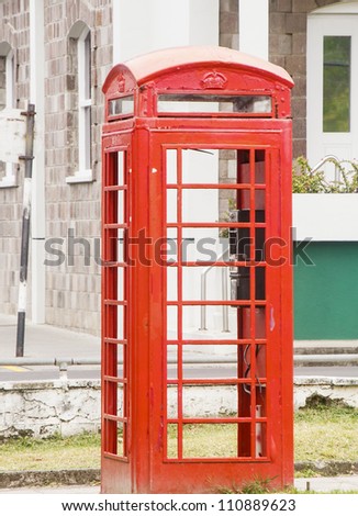 A vintage red wood phone booth by an old stone block building