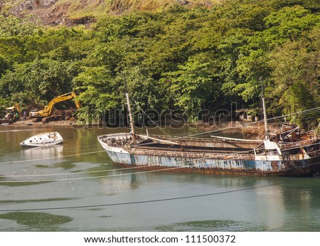 An old rusty blue ship sinking in a river next to a small white boat