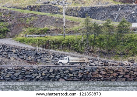 A commercial dump truck on a rock lined road zig-zagging up a hill on the shore in Alaska