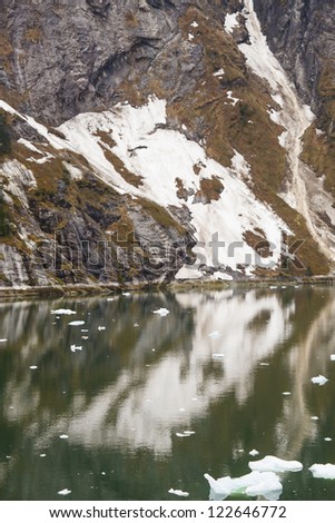 Snow on Rocky fjord by calm green water in Alaska