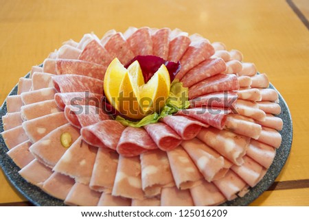 Assorted cold cuts arranged on a tray for serving with a cut orange in the center