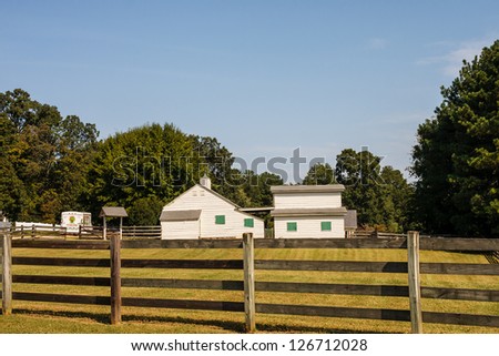 Yellow farm buildings with green shutters beyond wood rail fence