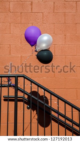 Three balloons tied to a black wrought iron railing with shadow on block wall background