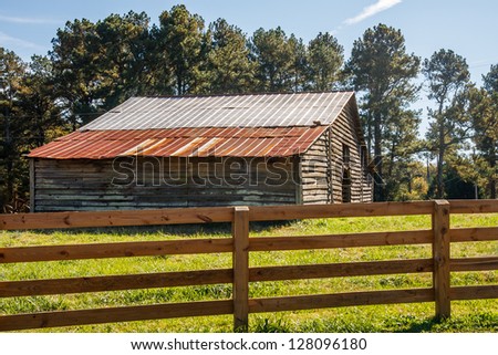 An old wood board and tin roof barn beyond a wood rail fence