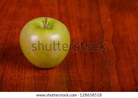 A single green Granny Smith apple on a wood table