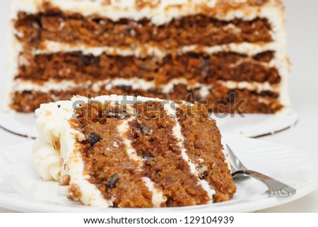 A slice of carrot cake on a plate with a fork. Half cake in the background