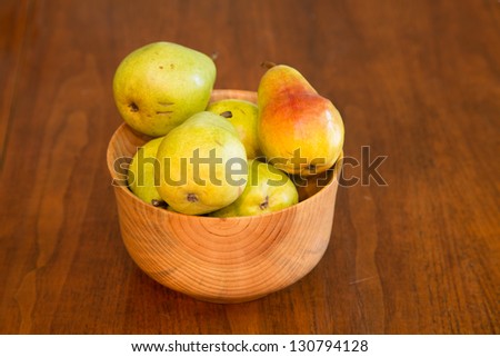 A hand made wood bowl on a wood table full of fresh, bartlett pears
