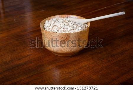 A bowl of fresh oatmeal ready to cook in a wood bowl with wood spoon on wood table