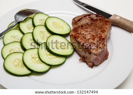 New York strip steak on a white plate with sliced cucumbers