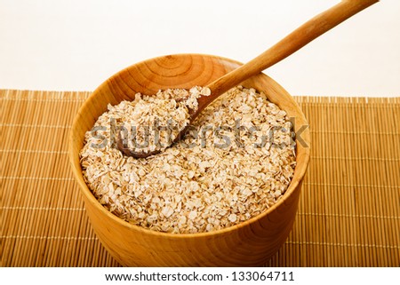 Fresh oats in a wood bowl with a wood spoon on a bamboo placemat