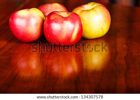 Four red macintosh apples on a shiny wood table with slight reflection