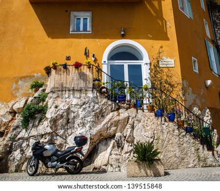 A modern motorcycle parked by an old stone staircase leading to an orange stucco villa