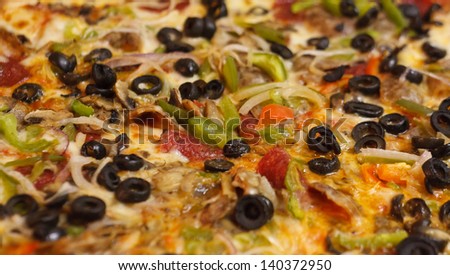 Closeup of a deluxe pizza with black olives and green peppers