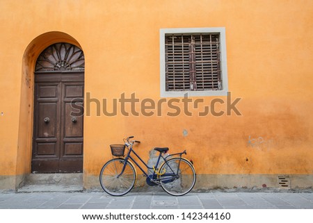 An old blue bike with basket and yellow lock on an orange wall with brown door