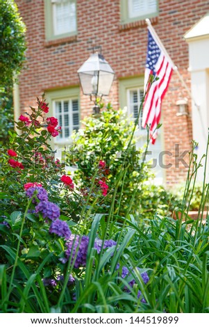 An American flag on a nice brick house with a lush spring garden in front