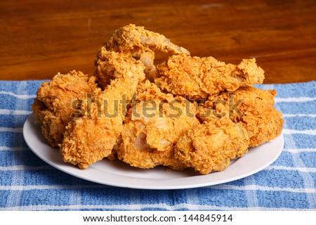 A plate of fresh, hot, crispy fried chicken on a blue plaid towel on a wood table