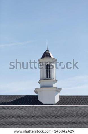A white wood cupola under blue skies on an asphalt shingle roof