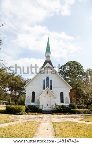 A small white, wooden church down sidewalk under nice sky
