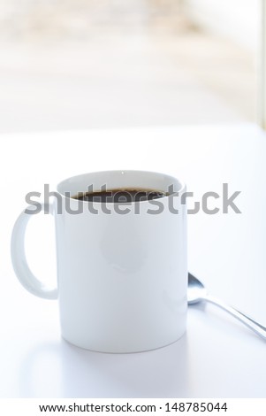 A white mug of coffee on a white counter in window light