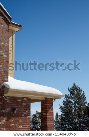 Snow on eave of brick home under clear blue skies