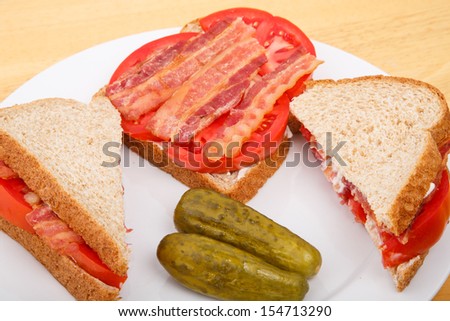 Fresh bacon and sliced tomato slices on a white plate with pickles