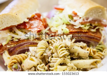 A fresh, italian, sub sandwich on a plate with pasta salad