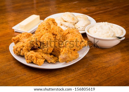 A dinner of fried chicken, mashed potatoes and biscuits with butter on wood table
