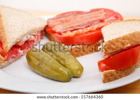 Fresh bacon and sliced tomato slices on a white plate with pickles