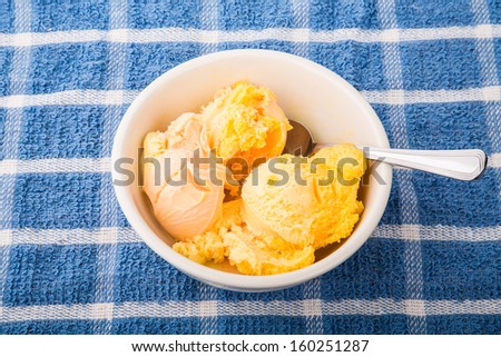 A white bowl of mango and peach sorbet on a blue plaid towel