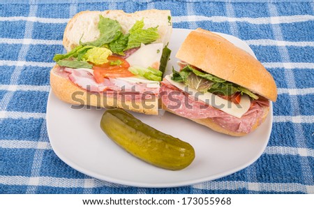 A fresh italian sub sandwich on a white plate with a whole dill pickle