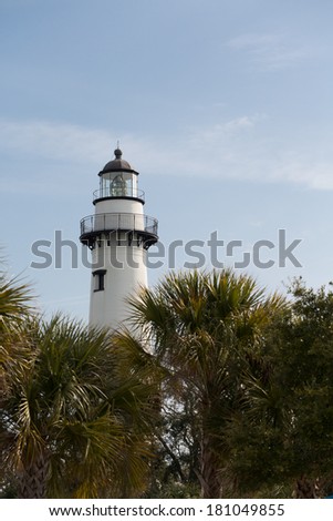 A white brick lighthouse rising out of green foliage under clear blue skies
