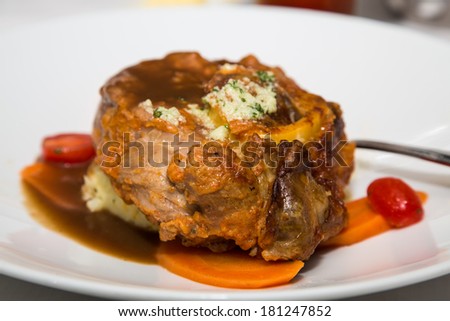 A fillet mignon steak on a white plate garnished with sauce, sliced carrots and blue cheese crumbles