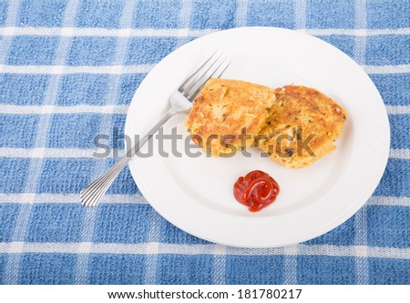 Two browned crab cakes on a white plate with fork and cocktail sauce on a blue towel