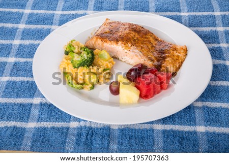 A plate of fresh, baked salmon with a broccoli, cheese and rice casserole and fresh cut fruit