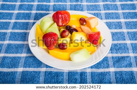 Fresh cut fruit on a white plate with strawberries, mango, pineapple, grapes, bananas, and melon