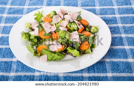 A fresh salad of greens, cucumber, sliced turkey and carrots in a white plate