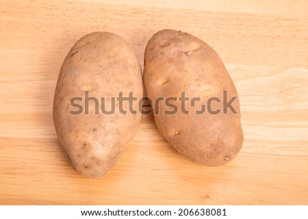 Two raw Idaho baking potatoes on a wood cutting board