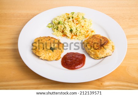 Two browned crab cakes in white plate with cocktail sauce and vegetable rice