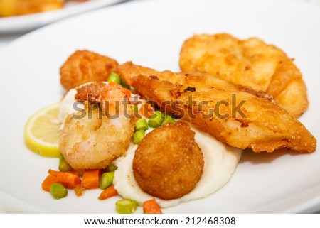 Fried shrimp and fish on a plate with sauce, lemon and vegetables