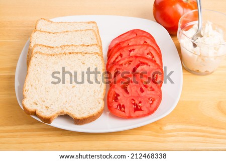 Slices of whole grain bread and sliced tomatoes on a plate for tomato sandwiches