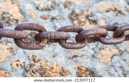 A length of heavy, steel, rusty chain over a stone and masonry wall