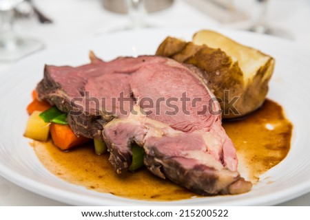 Slab of rare prime rib on a bed of vegetables with a baked potato