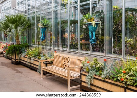 Empty wood benches along a sidewalk outside a greenhouse in a public garden