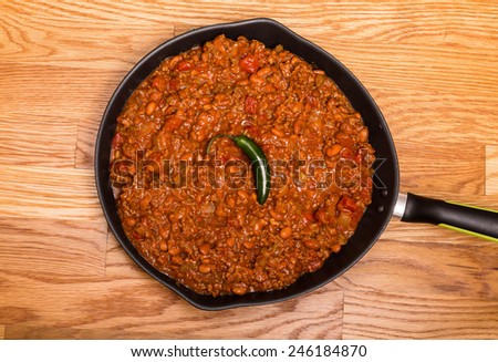 Chili with meat and beans in a black iron skillet on a wood table