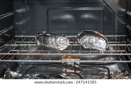 Two baked potatoes on a rack in an oven