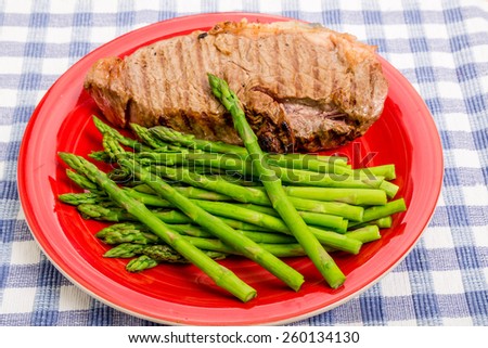 Grilled strip steak on a red plate with asparagus