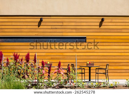 Garden by tables and chairs with mustard and ketchup bottles by a wood wall of a restaurant