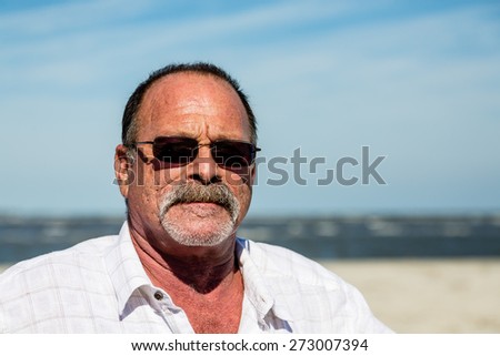 An old guy on the beach wearing sunglasses